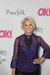 a woman in a purple top and black pants posing on a red carpet