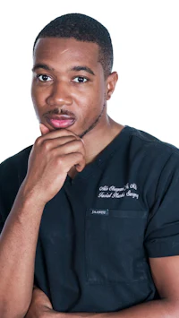 a man in a black scrub shirt posing with his hand on his chin