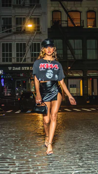 a woman in a leather skirt and hat walking down a cobblestone street
