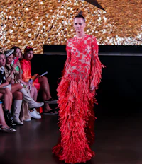 a model walks down the runway in a red dress with feathers