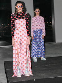 two women standing on a runway in colorful outfits